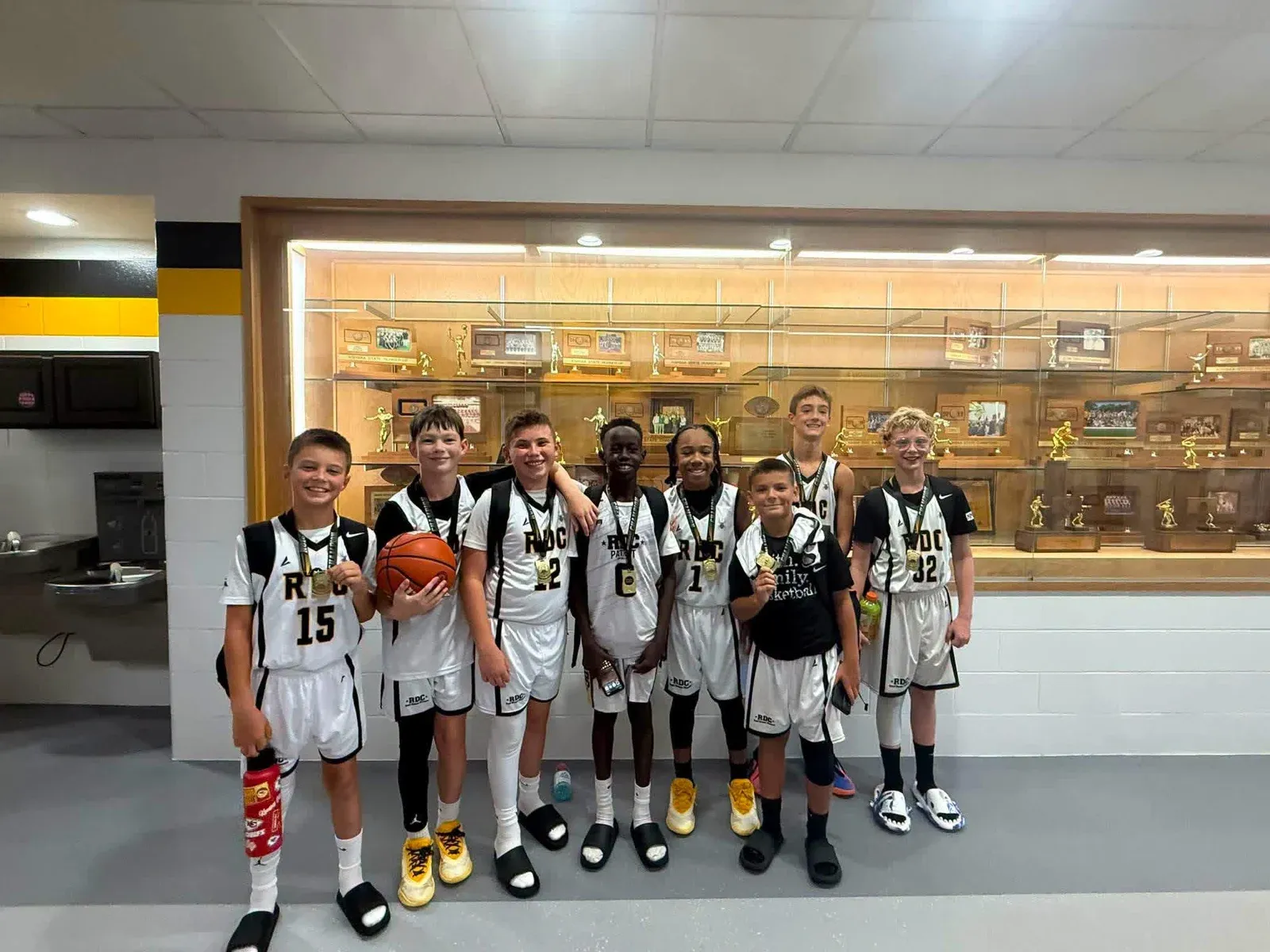 RDC basketball team gathered in front of a trophy case